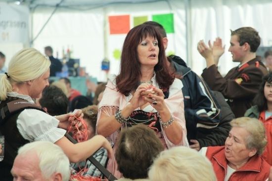 Eine Frau in traditioneller Kleidung spricht zu einer Menschenmenge auf einem Festival, während andere zuhören und applaudieren.
