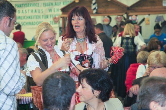Zwei Frauen in traditioneller Kleidung unterhalten sich bei einer überfüllten Veranstaltung, wobei eine eine rote Schleife hält.