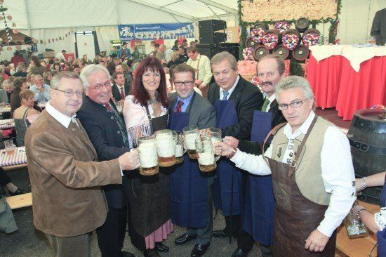 Eine Gruppe von Menschen in formeller Kleidung hebt Biergläser in einer festlichen Umgebung.