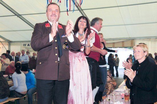 Ein Mann in Uniform und eine Frau in einem rosa Kleid klatschen in einem Zelt mit anderen Leuten.