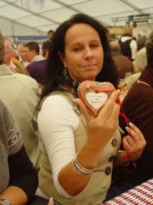 Eine Frau in einer beigen Weste hält einen herzförmigen Keks mit einer Nachricht darauf bei einer überfüllten Veranstaltung.