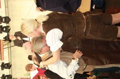 Eine Frau in traditioneller bayerischer Kleidung küsst einen Mann auf die Wange, während andere zusehen.