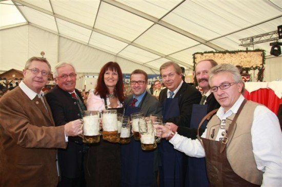 Eine Gruppe von Menschen in formeller Kleidung hält große Bierkrüge in einem Zelt hoch.
