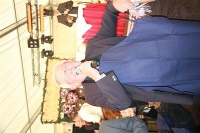 Ein älterer Mann in einem blauen Anzug und mit Brille hält ein Mikrofon und singt in einer festlichen Umgebung mit einer Weihnachtsdekoration im Hintergrund.
