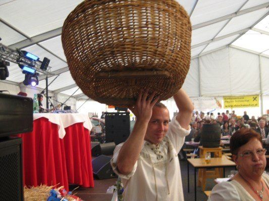Ein Mann hält einen großen Korb aus Weide über seinem Kopf in einem Zelt-Event, während eine Menge Menschen zuschaut.