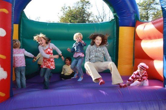Mehrere Kinder spielen in einem farbenfrohen aufblasbaren Hüpfhaus, einige springen und andere sitzen auf dem Boden.