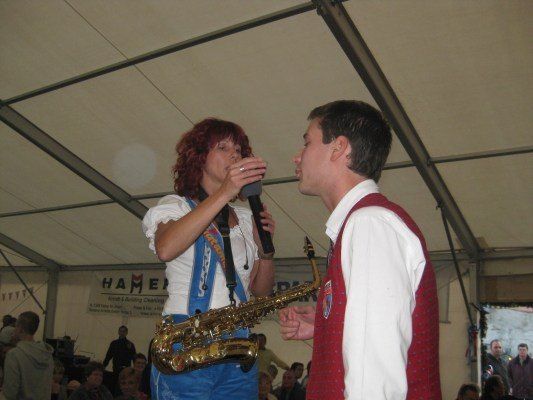 Eine Frau mit roten Haaren singt in ein Mikrofon, während ein Mann Saxophon spielt. Sie treten auf einer Bühne auf, während eine große Menge zuschaut.