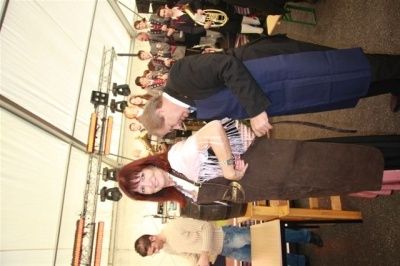 Ein Mann und eine Frau stehen zusammen in einem Raum mit einer Band im Hintergrund, der Mann scheint das Kleid der Frau zu justieren.