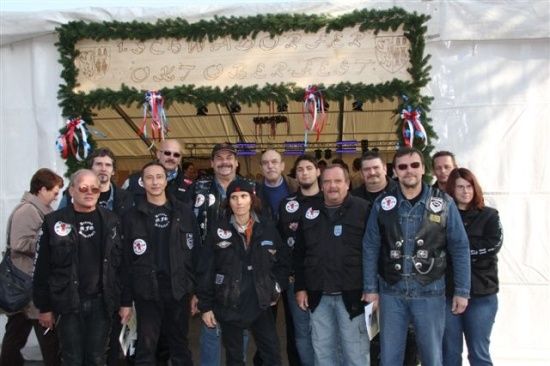 Eine Gruppe von Menschen in schwarzen Jacken mit Aufnähern und einigen mit Mützen posiert für ein Foto vor einem geschmückten Zelt.