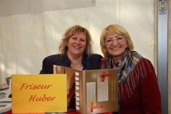 Zwei Frauen lächeln und posieren für ein Foto mit einem Buch mit dem Titel 'Friseur Huber'.
