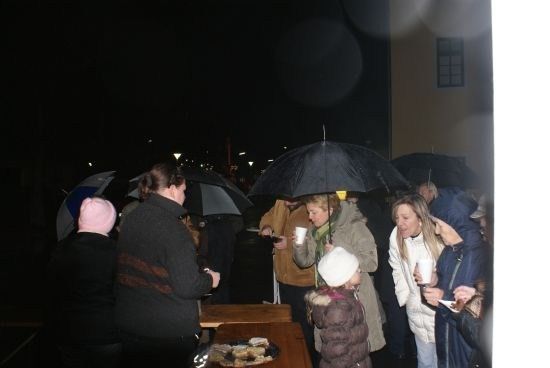 Eine Gruppe von Menschen versammelt sich bei Nacht unter Regenschirmen und genießt Essen und Getränke. Ein Kind hält einen Becher.