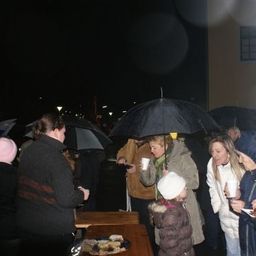 Eine Gruppe von Menschen versammelt sich bei Nacht unter Regenschirmen und genießt Essen und Getränke. Ein Kind hält einen Becher.