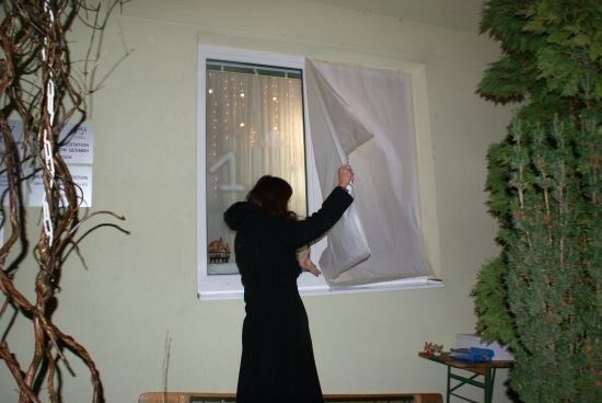 Eine Frau in einem schwarzen Mantel zieht einen weißen Vorhang über ein Fenster, auf dem die Nummer 1 zu sehen ist.