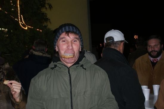 Ein Mann in einer grünen Jacke und einer Mütze isst etwas, während andere um ihn herum sind.