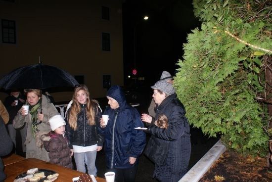 Eine Gruppe von Menschen, darunter eine Frau mit einem Regenschirm, steht an einem Tisch mit Essen und Getränken an einem regnerischen Abend.