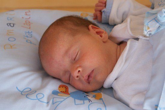 Ein Baby schläft friedlich auf einem Bett mit einer blau-weißen Decke mit den Worten 'Piti Lapins' und 'Ree' darauf.