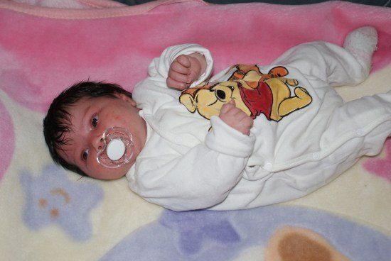 Ein Baby mit einem Schnuller liegt auf einer Decke mit Winnie-the-Pooh-Aufdruck.