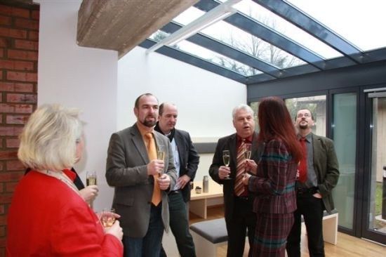 Eine Gruppe von Menschen in formeller Kleidung steht in einem Raum mit Glasdecke und hält Weingläser.