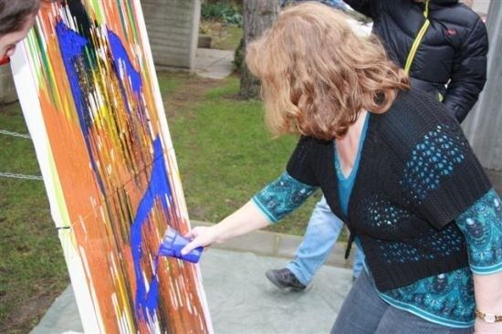 Eine Frau malt auf eine große Leinwand mit blauer Farbe, während eine weitere Person hinter ihr steht.