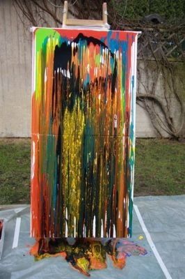 Ein abstraktes Gemälde mit leuchtenden Farben wie Rot, Gelb und Blau wird auf einem Staffelei in einer Außenumgebung ausgestellt.