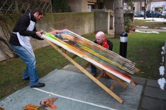 Zwei Männer malen ein großes Gemälde auf einem Staffelei im Garten. Ein Mann steht und der andere kniet.