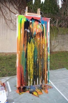 Ein abstraktes Gemälde mit leuchtenden Farben, möglicherweise eine menschliche Figur darstellend, wird auf einem Staffelei im Freien ausgestellt.