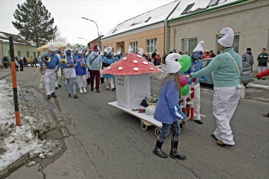 Eine Gruppe von Menschen in blauer Gesichtsbemalung und Kostümen geht die Straße entlang, einige tragen Musikinstrumente und einen pilzförmigen Wagen.