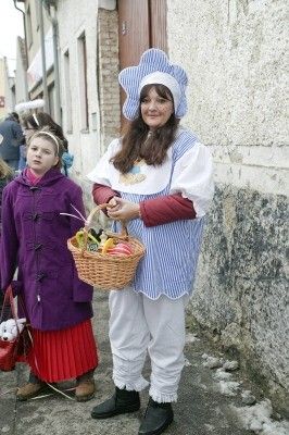 Eine Frau in traditioneller Kleidung hält einen Korb mit Ostereiern neben einem jungen Mädchen in einem lila Mantel auf einer Straße.