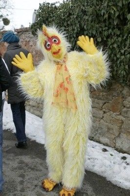 Eine Person in einem gelben Hühnerkostüm mit roten Augen und gelben Handschuhen steht auf einer verschneiten Straße.