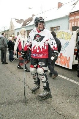 Eine als Pirat verkleidete Person in Rollschuhen und mit einem Hockeyschläger läuft auf einer Straße mit Zuschauern und einem Van im Hintergrund.