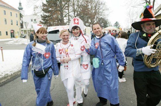 Eine Gruppe von Menschen in medizinischen Kostümen und blauen Gewändern geht auf einer verschneiten Straße bei einem Umzug.