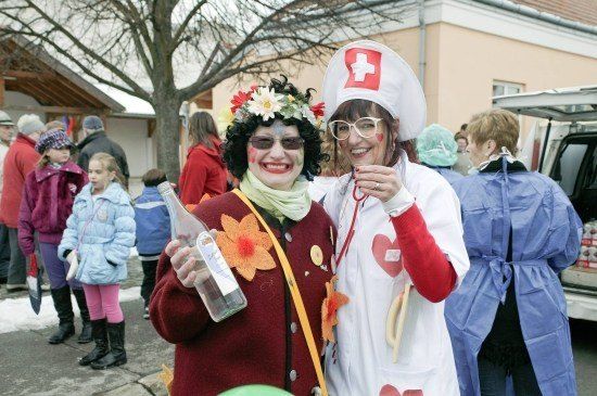 Zwei Frauen in Kostümen, eine als Krankenschwester und die andere als Blume, stehen zusammen in einer festlichen Außenumgebung.