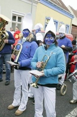 Eine Gruppe von Menschen in blauen Kostümen mit weißen Hüten und blauer Gesichtsbemalung marschiert in einem Umzug und hält Musikinstrumente in den Händen.