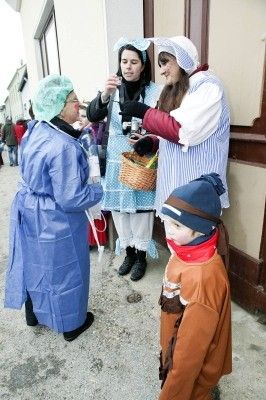 Eine Gruppe von Menschen in Kostümen, einer hält einen Korb, ein anderer eine Flasche, und ein Kind vor ihnen.