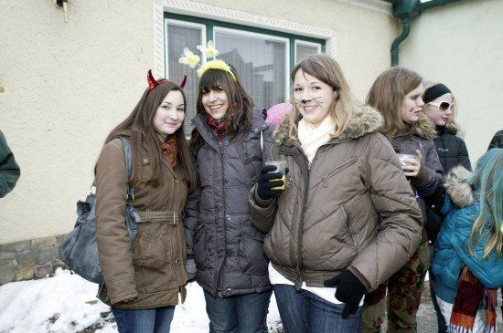 Eine Gruppe von Frauen in Winterkleidung, einige mit Gesichtsbemalung, stehen vor einem Gebäude in einem verschneiten Gebiet.