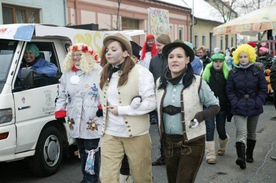 Eine Gruppe von Menschen in Kostümen geht eine Straße entlang, mit einem Van und einem Zelt im Hintergrund.