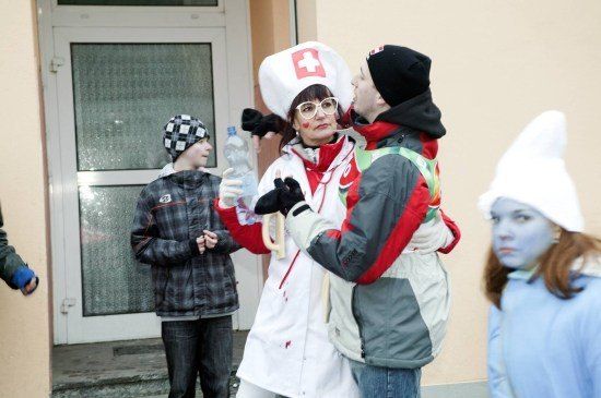 Eine Gruppe von Menschen in Kostümen, eine als Krankenschwester, eine andere als Zombie und ein Kind in einer karierten Jacke, stehen vor einem Gebäude.
