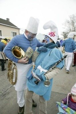 Zwei Personen in blauen Kostümen und Gesichtsbemalung halten Musikinstrumente, möglicherweise eine Tuba und eine Klarinette, während sie in einem Außenbereich mit anderen Personen stehen.