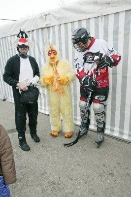 Drei Personen in Kostümen stehen vor einer gestreiften Wand. Eine Person trägt ein Hühnerkostüm, eine andere eine Katzenmaske und die dritte ein Hockey-Trikot mit Helm.