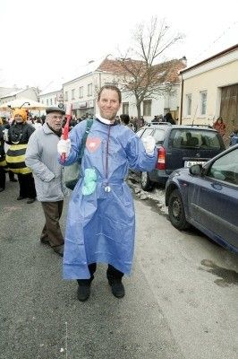 Ein Mann in einem blauen Schutzanzug steht auf einer Straße mit Menschen und Autos im Hintergrund.