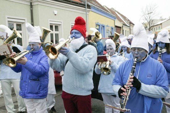 Eine Gruppe von Menschen, die in blaue Gesichtsbemalung und weiße Hüte gekleidet sind, spielen Musikinstrumente bei einem Umzug.