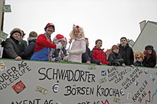 Eine Gruppe von Menschen in Kostümen mit einem Banner mit dem Text Schwadorfer Borsen Kroche steht vor einem Gebäude.