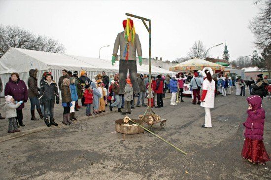 Eine Menschenmenge versammelt sich um eine große Marionette auf einem Wagen, mit einem Lagerfeuer davor. Einige tragen Winterkleidung und Mützen.
