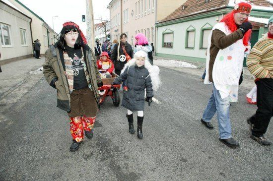 Eine Gruppe von Menschen in Kostümen geht eine Straße entlang, einer zieht ein Kind in einem Wagen.