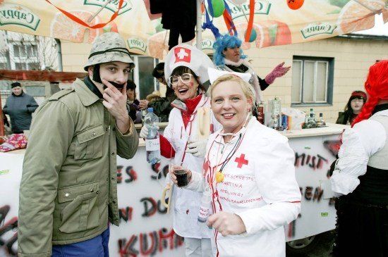 Eine Gruppe von Menschen in Kostümen, darunter ein Soldat und zwei Frauen in Krankenschwesternuniformen, steht vor einem Zelt mit einem Banner.