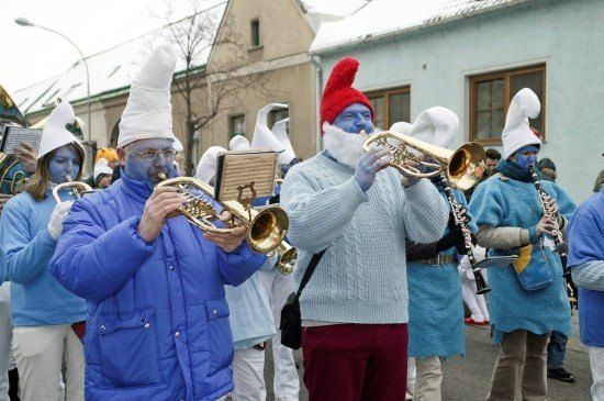 Eine Gruppe von Menschen in blauen Kostümen mit weißen Hüten und blauer Gesichtsbemalung spielt Musikinstrumente bei einem Umzug.