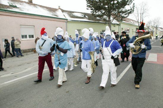 Eine Gruppe von Menschen in blauen Kostümen und weißen Hüten marschiert auf der Straße und spielt Musikinstrumente.
