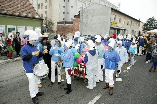 Eine Gruppe von Menschen in blau-weißen Kostümen mit blauer Gesichtsbemalung, die mit Musikinstrumenten und Luftballons in einem Umzug marschieren.
