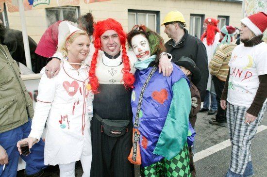 Eine Gruppe von Menschen in Kostümen, zwei davon in Clown-Kostümen, posiert für ein Foto auf einer Straße.