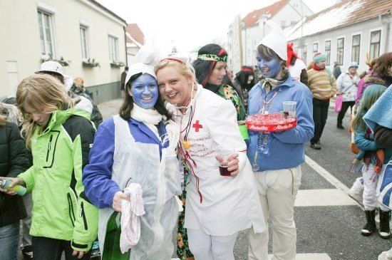 Eine Gruppe von Menschen in Kostümen, darunter eine Krankenschwester und eine Fee, steht während eines Umzugs auf einer Straße.